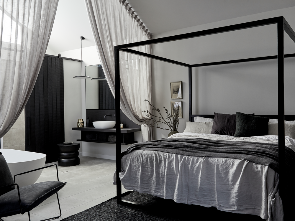 Half Wood Smoke eggshell in a modern bedroom with a four-poster bed, black and white decor, and a bathroom in the background.