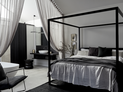 Half Wood Smoke eggshell in a modern bedroom with a four-poster bed, black and white decor, and a bathroom in the background.