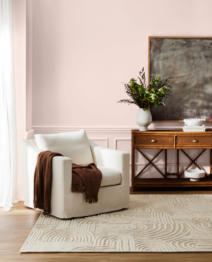 SYDNEY HARBOUR PAINT Co Wall color is PETAL PINK_ Living room with a white armchair, wooden console table, and abstract painting on a pink wall.